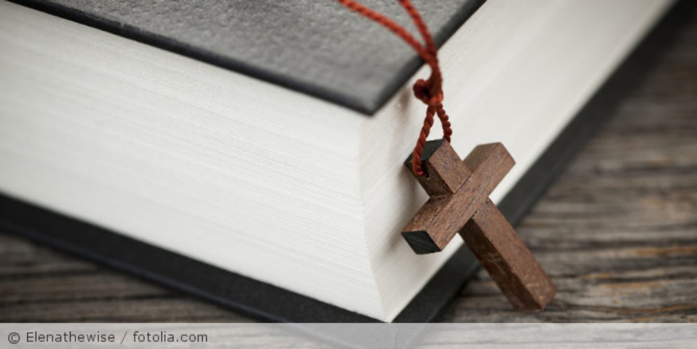 Kreuzkette die an einem roten Faden hängt, liegt an der Bibel.