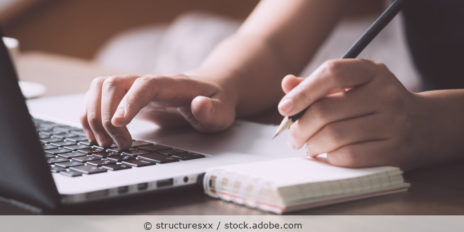 Frau schreibt Notiz auf einen Notizublog, der neben einem Laptop liegt