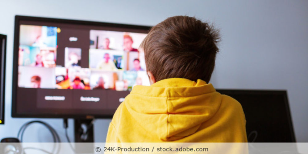 Junge im gelben Hoody sitzt vor einem Computer und nimmt an einer Videokonferenz teil