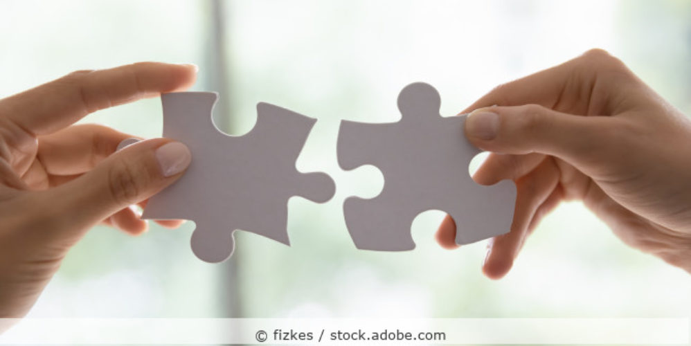 zwei Hände setzen 2 Puzzleteile in der Luft zusammen