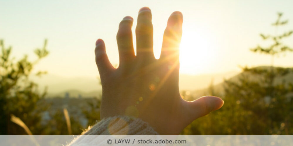 Eine geöffnete Hand greift nach der Sonne am Horizont.