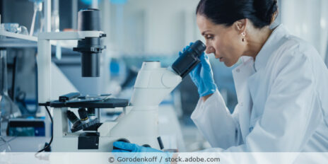 Eine Frau im weißen Kittel schaut in einem Labor in ein Mikroskop.