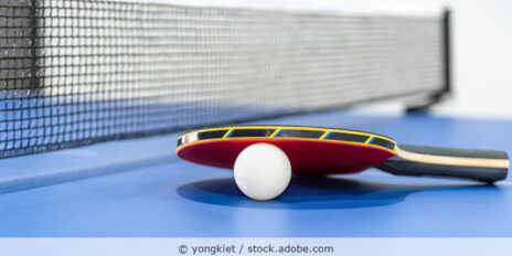 Tischtennisschläger und Tischtennisball liegen auf einer blauen Tischtennisplatte.