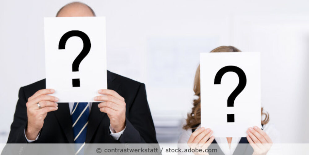 Ein Mann und eine Frau in Businesskleidung halten Schilder mit einem aufgedruckten Fragezeichen vor ihre Gesichter.