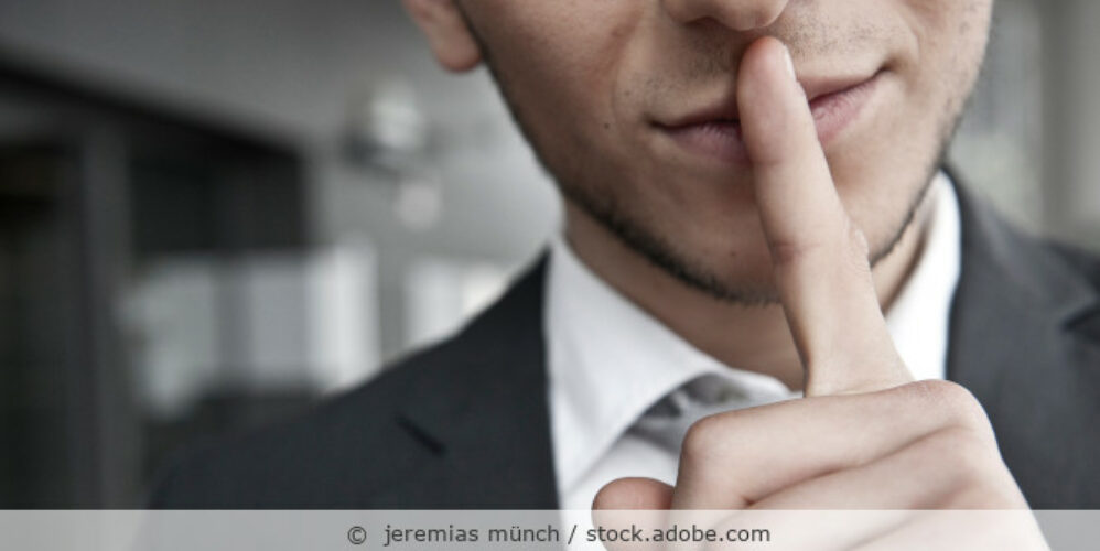 Mann im Anzug legt den Finger auf den Mund als Zeichen zu schweigen.
