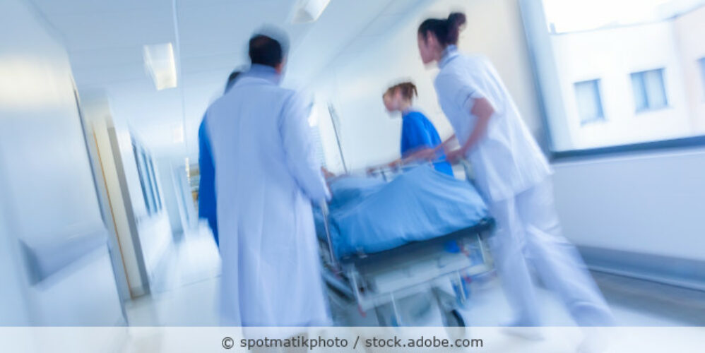 Medizinisches Personal schiebt einen Patienten im Krankenbett einen Flur entlang.