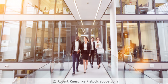 Vier Geschäftsleute oder Kollegen laufen einen Flur in einem Bürogebäude entlang.