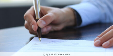 Mann unterscheibt ein Dokument mit einem Kugelschreiber am Schreibtisch.