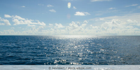 Die Sonne spiegelt sich am Horizont auf dem blauen Meerwasser.