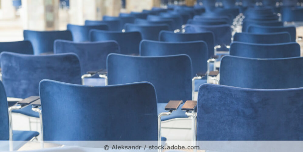 Stühle mit blauem Bezug stehen in Stuhlreihen in einem großen Konferenzraum.