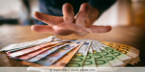 Hand greift nach Euro-Geldscheinen, die auf einem Tisch liegen.