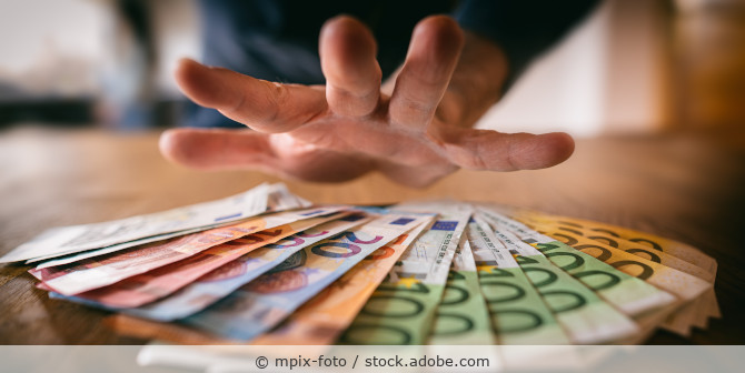 Hand greift nach Euro-Geldscheinen, die auf einem Tisch liegen.