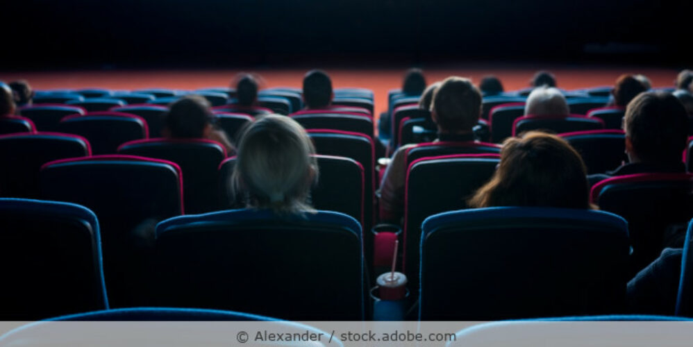 Zuschauer sitzen in einem dunklen Kinosaal mit Blick zur Leinwand.