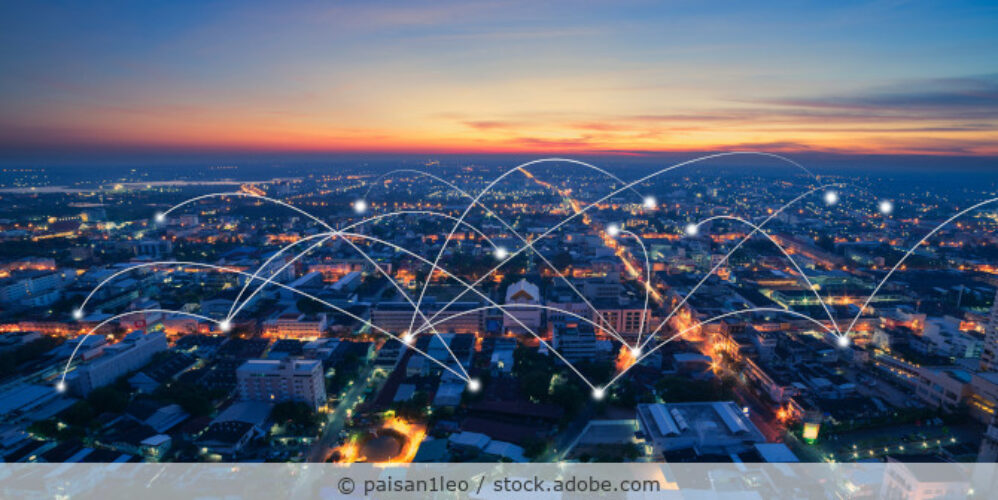 Ansicht einer Stadt von oben in der Abenddämmerung bei der viele Verbindungen zwischen Punkten eingezeichnet sind, um eine Smart City zu veranschaulichen.