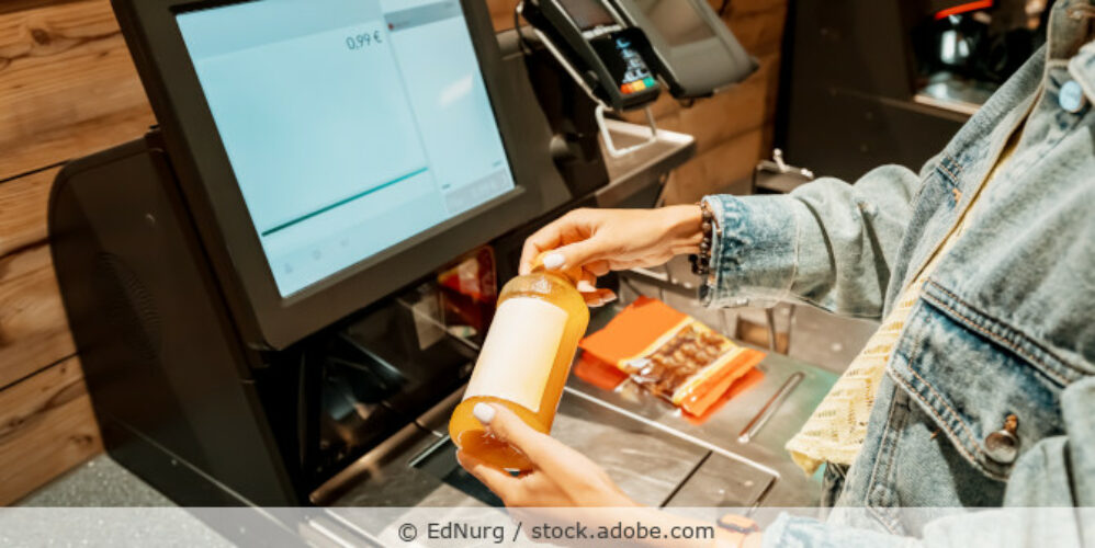 Eine Kundin scannt und bezahlt eine Flasche Saft in einem Supermarkt an einem automatischen Selbstbedienungs-Kassenterminal.
