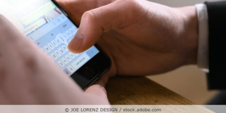 Mann in Business-Kleidung tippt eine Nachricht ins Handy (Chat); Detailaufnahme vom Handy in der Hand.