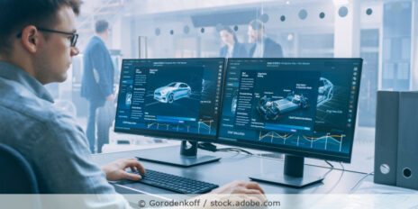 Entwickler sitzt im Büro vor zwei Computerbildschirmen auf denen CAD-Zeichnungen von Autos zu sehen sind.